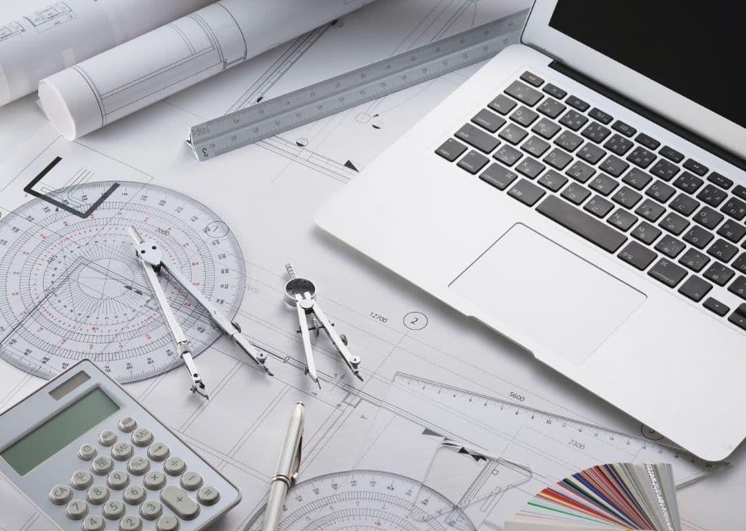 Engineering drawings, drafting instruments and a laptop on a desk