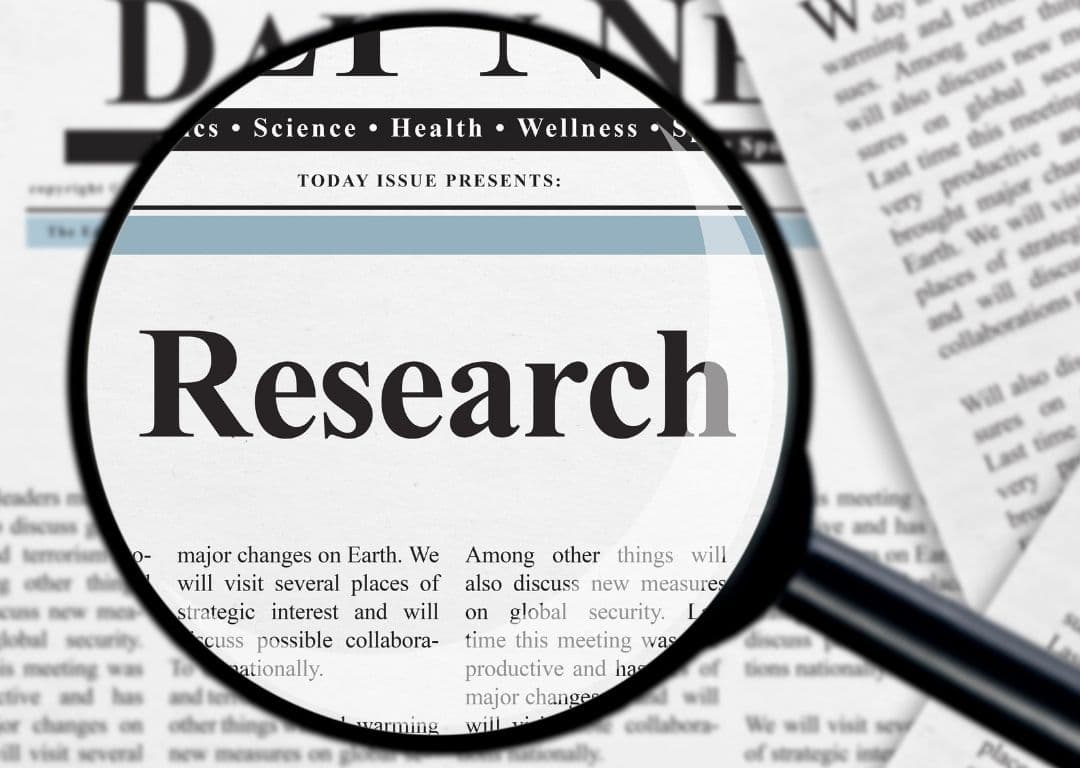 Magnifying glass over a newspaper highlighting the word “Research”